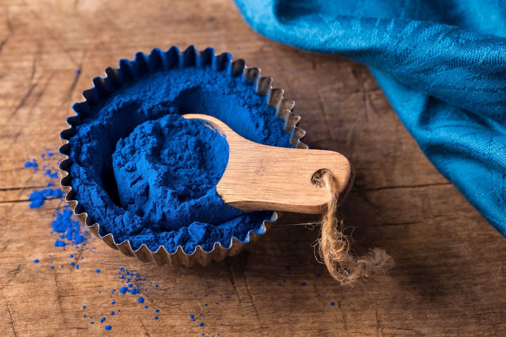 Blaues Pulver in einer Metallform mit Holz-Löffel. Auf Holzuntergrund, blaues Tuch.