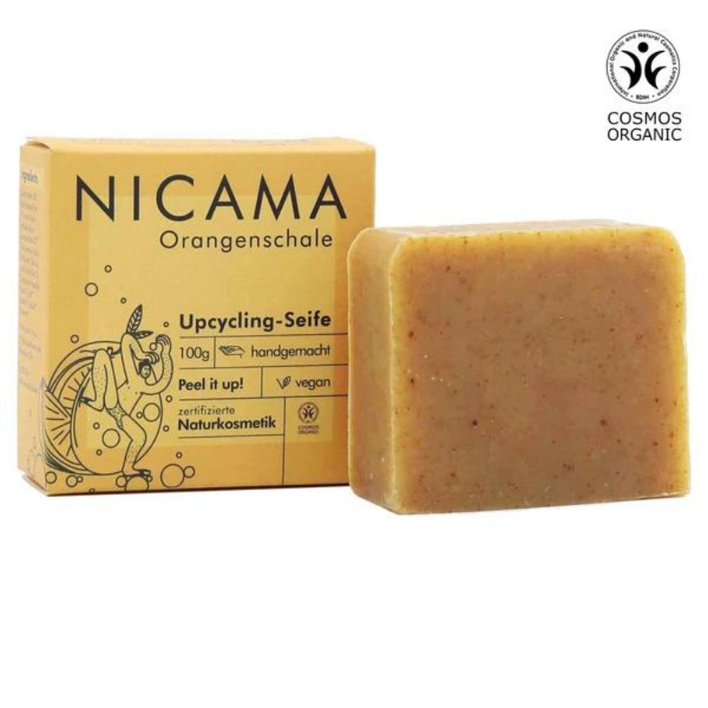 Seife und Verpackung. Aufschrift: NICAMA, Orangenschale, Upcycling-Seife, 100g, handgemacht, vegan, zertifizierte Naturkosmetik. COSMOS ORGANIC.