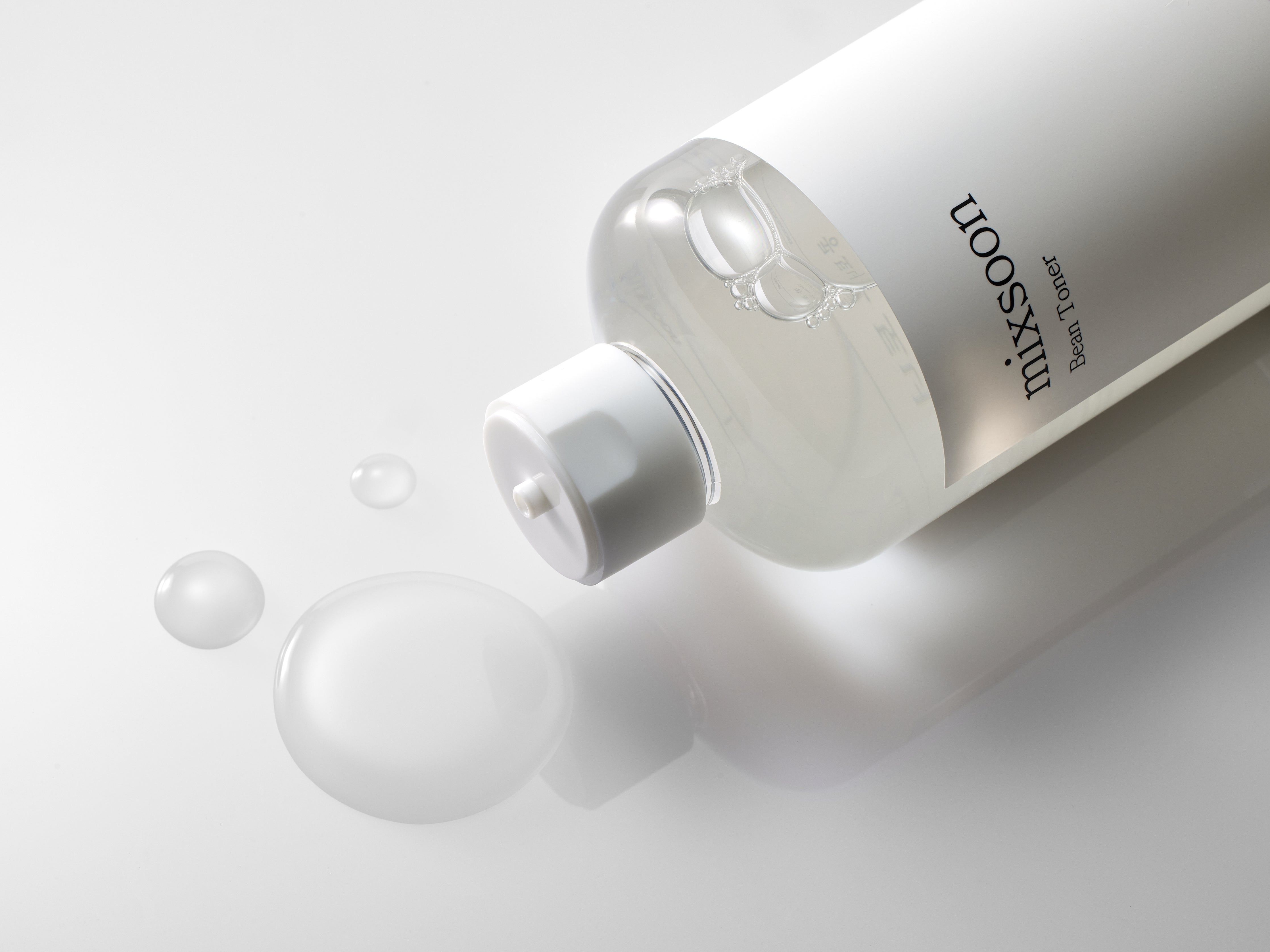 Eine Flasche mixsoon Bean Toner liegt auf einer Oberfläche. Daneben befinden sich einige Tropfen Flüssigkeit.
