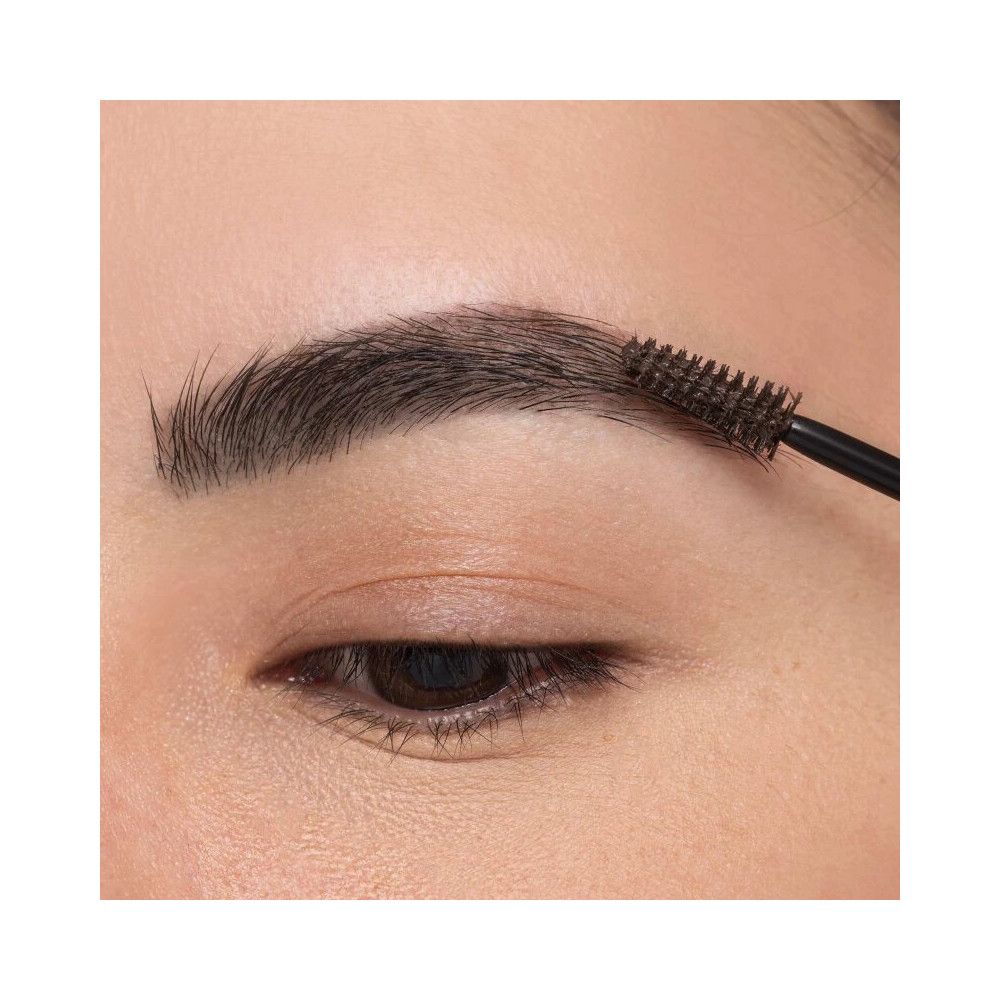 Auge mit Augenbraue, die mit einer Bürste bearbeitet wird. Die Augenbraue ist dunkel und buschig.