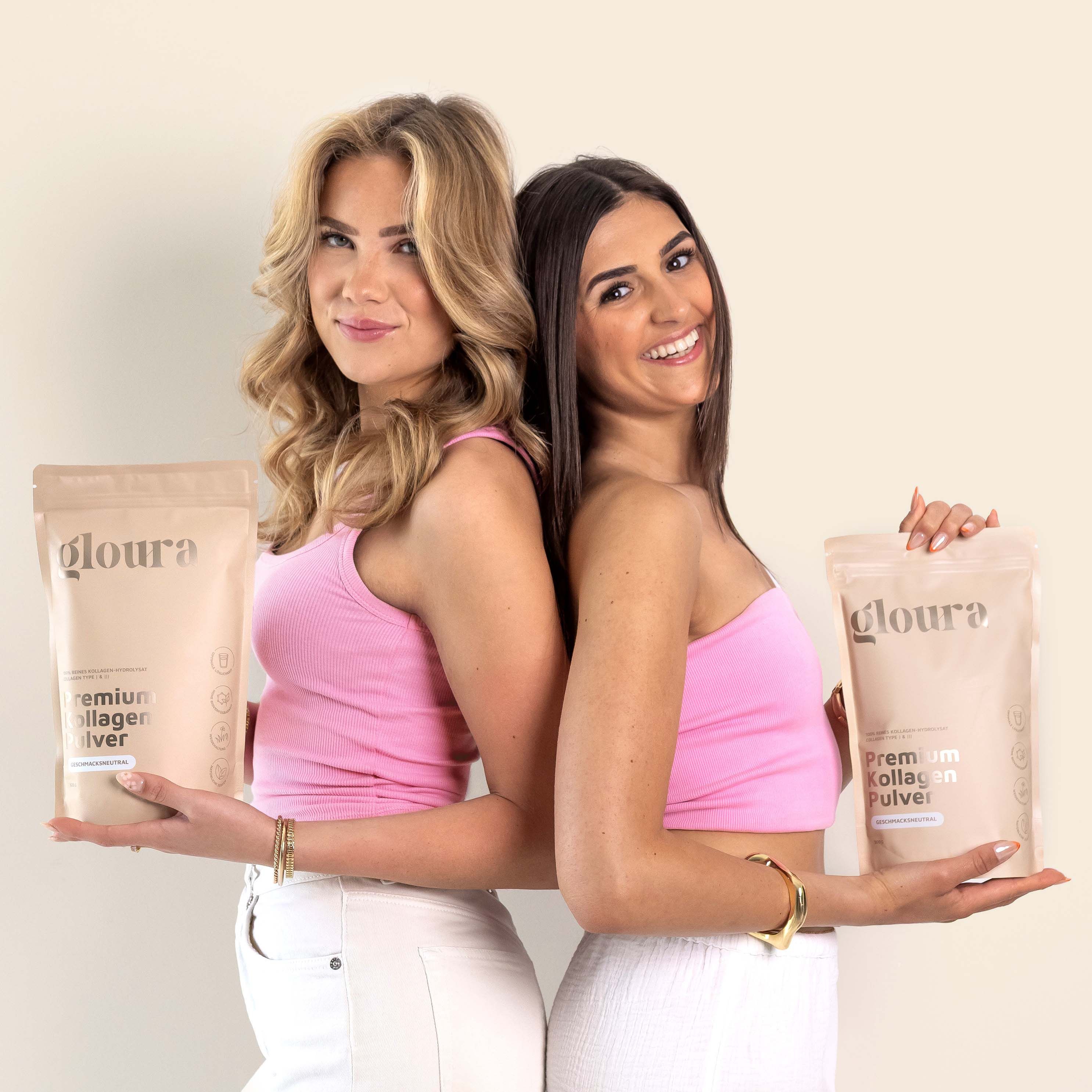 Zwei Frauen halten "gloura" Kollagen Pulver Packungen. Beide tragen rosa Tops und stehen Rücken an Rücken.