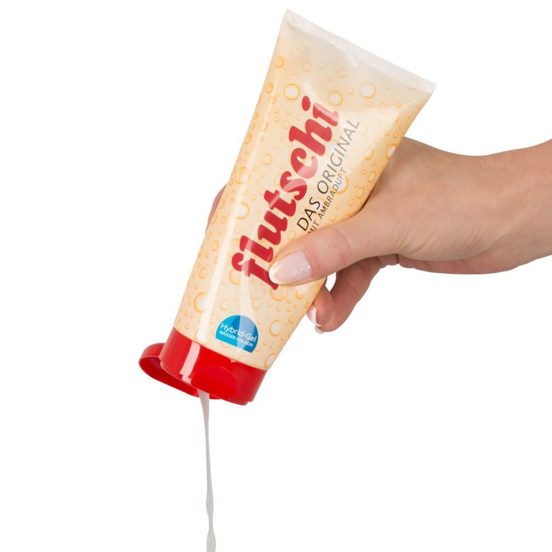 Hand hält Tube 'Flutschi - das Original'. Gel fließt aus der Öffnung. Roter Deckel. Beige Tube.