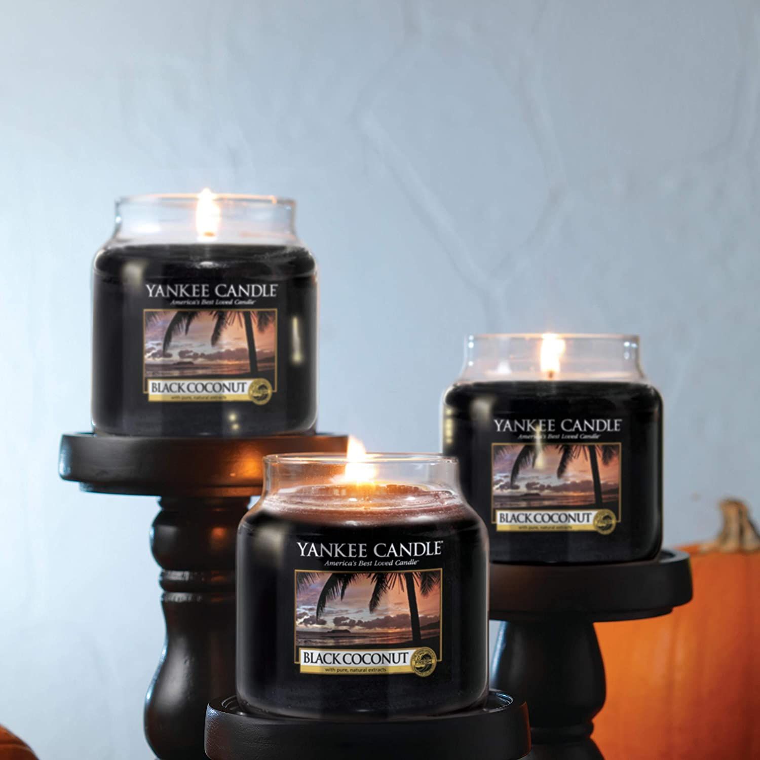 Drei brennende Kerzen in Gläsern auf schwarzen Podesten. Auf den Etiketten steht "Yankee Candle Black Coconut".