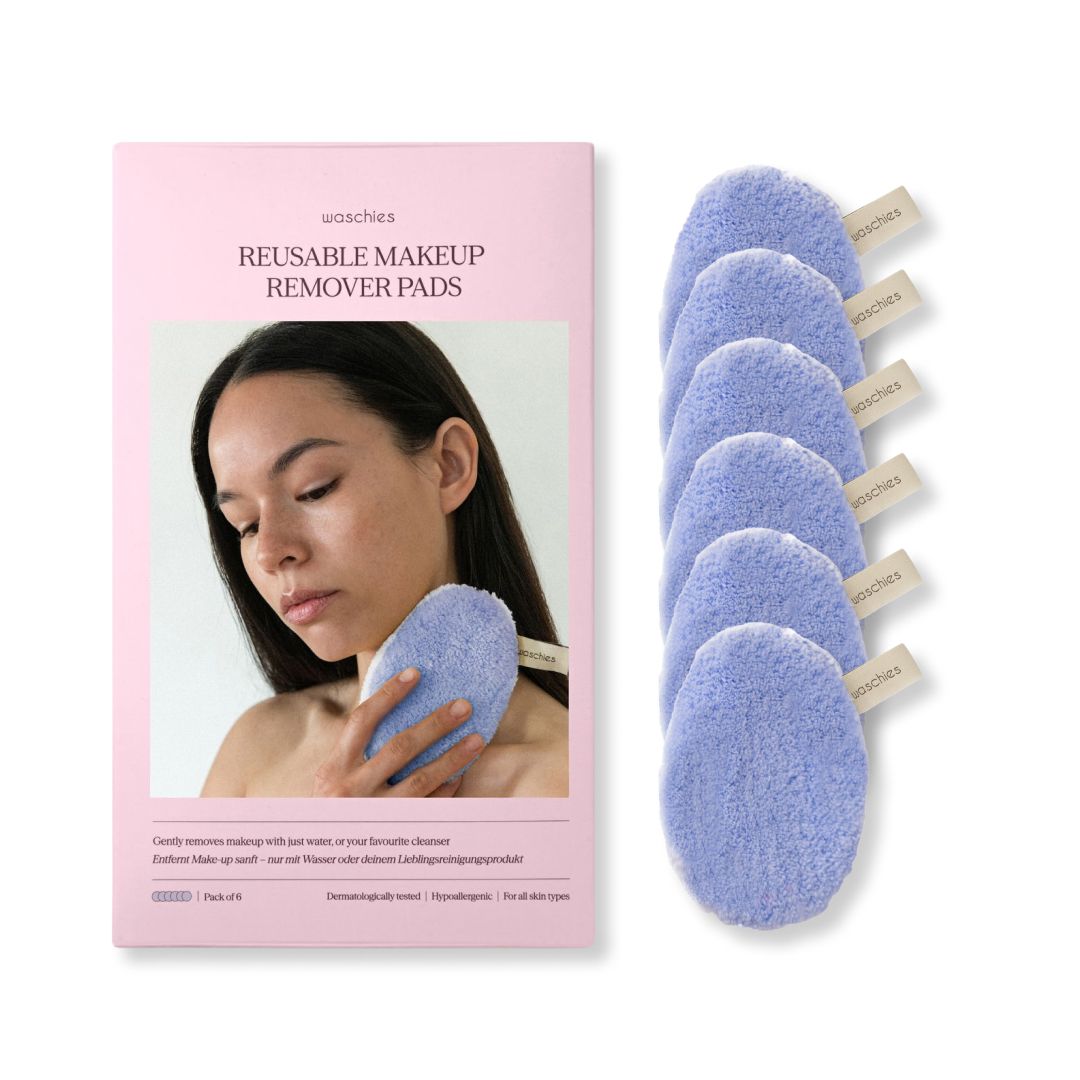 Eine Frau hält ein blaues Abschminkpad neben einer Packung. Auf der Packung steht: Waschies, Reusable Makeup Remover Pads.