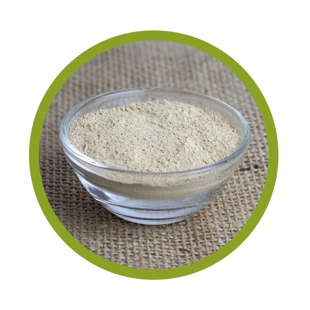 Runde, transparente Glasschale mit hellem Pulver, vor grobem Stoffhintergrund.