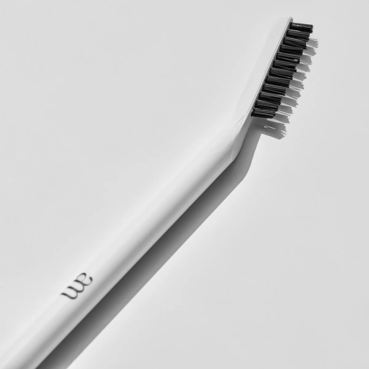 Pettine per sopracciglia bianco con logo AM. Setole nere. Ombra su sfondo bianco.