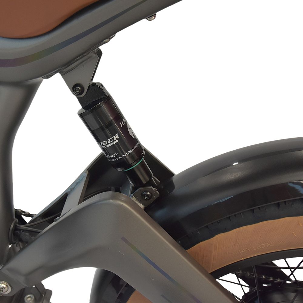 Nahaufnahme des hinteren Stoßdämpfers einer grauen Elektrodirtbike. Schwarze Details und Aufschrift 'SHOCK'.