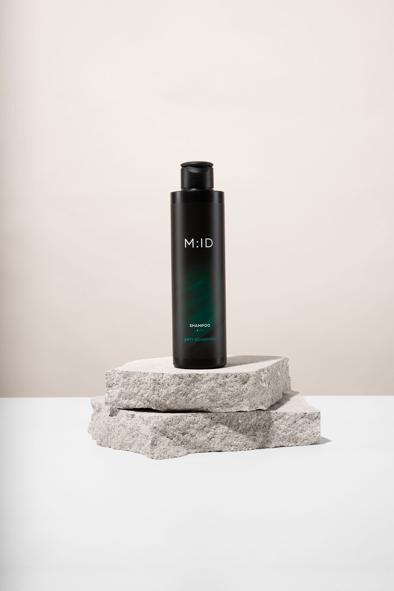 Schwarze Shampoo-Flasche mit weißem "M:ID"-Logo. Auf Steinblöcken platziert. Darunter "SHAMPOO" und "ANTI-SCHUPPEN" in Weiß.