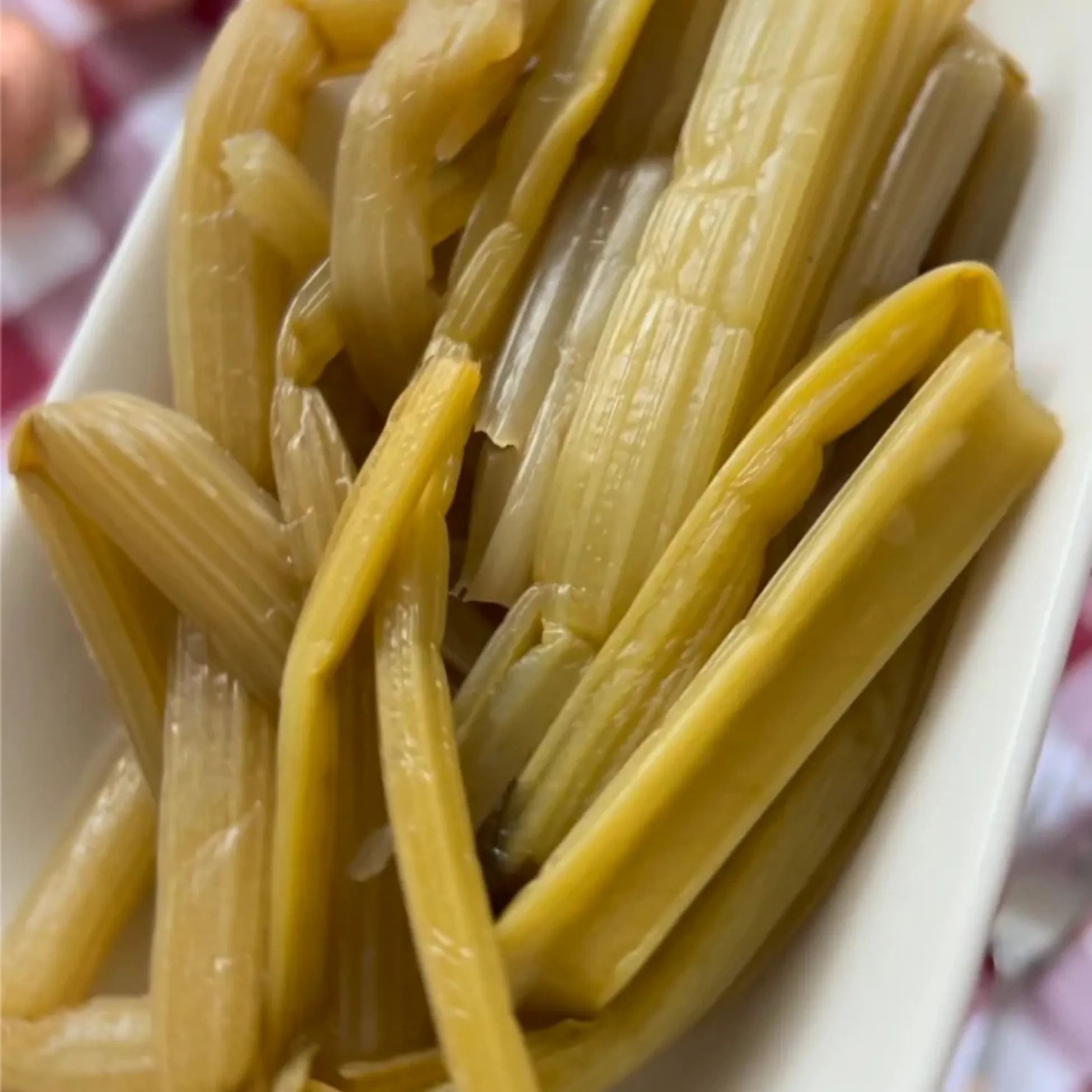 Nahaufnahme von eingelegten Pezik-Stangen in einer weißen Schale. Die Stangen sind gelblich-grün und leicht transparent.