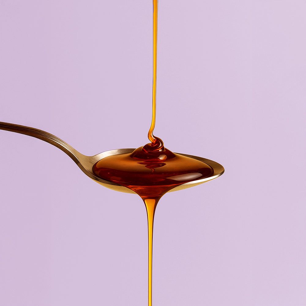 Braune Flüssigkeit fließt von einem Löffel. Hintergrund: hellviolett.