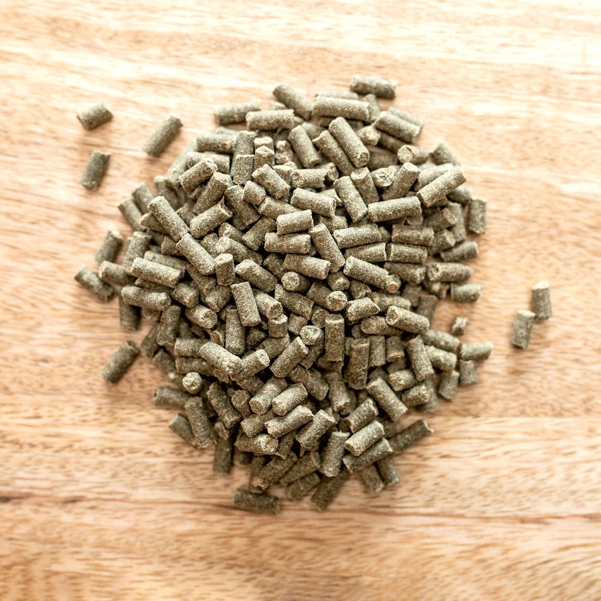 Haufen von zylindrischen, grün-braunen Pellets auf Holzuntergrund. Einzelne Pellets verstreut. Nahaufnahme.