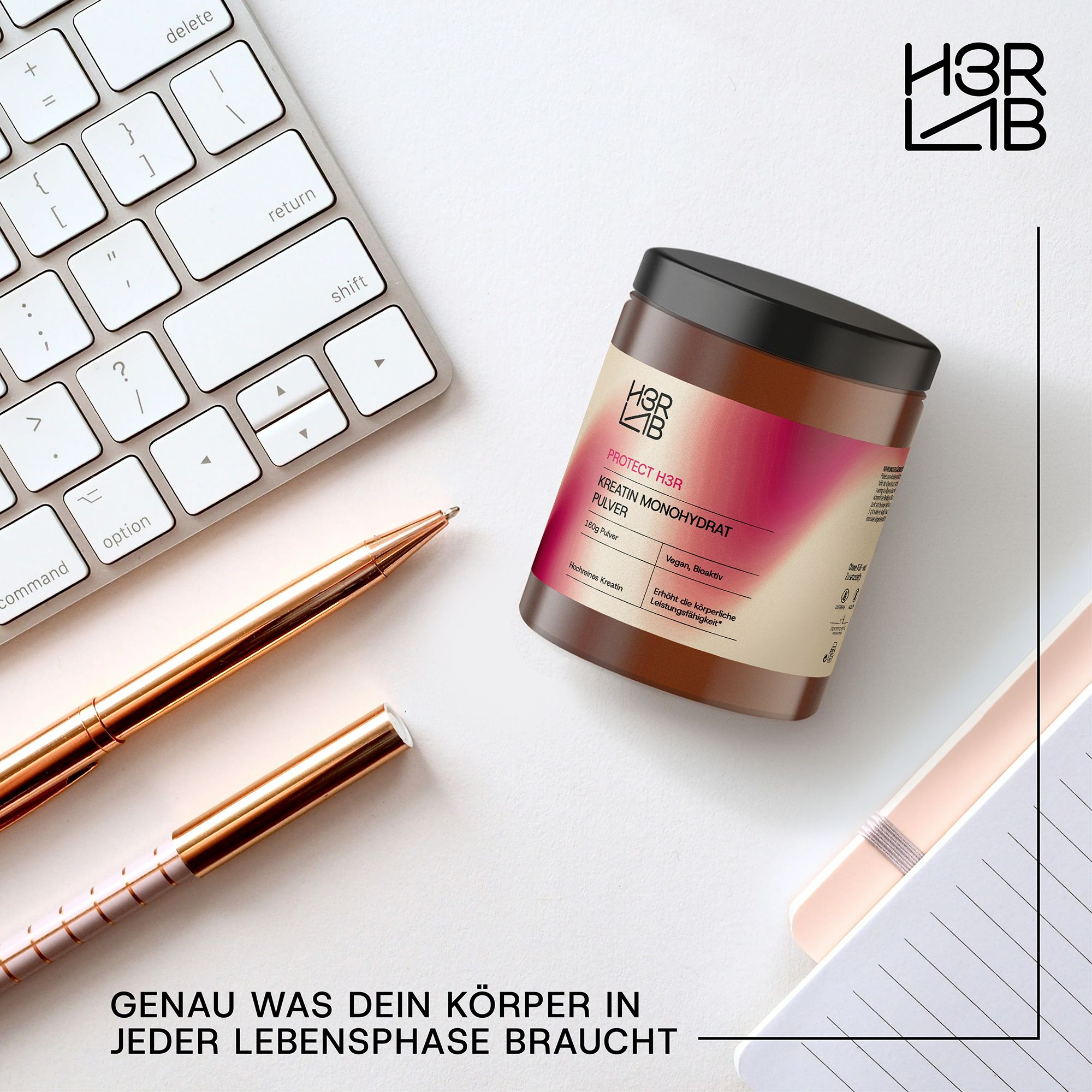 Braune Dose mit schwarzem Deckel, H3R LAB, Kreatin Monohydrat Pulver. Auf Schreibtisch mit Tastatur, Stiften und Notizbuch. Text: Genau was dein Körper braucht.