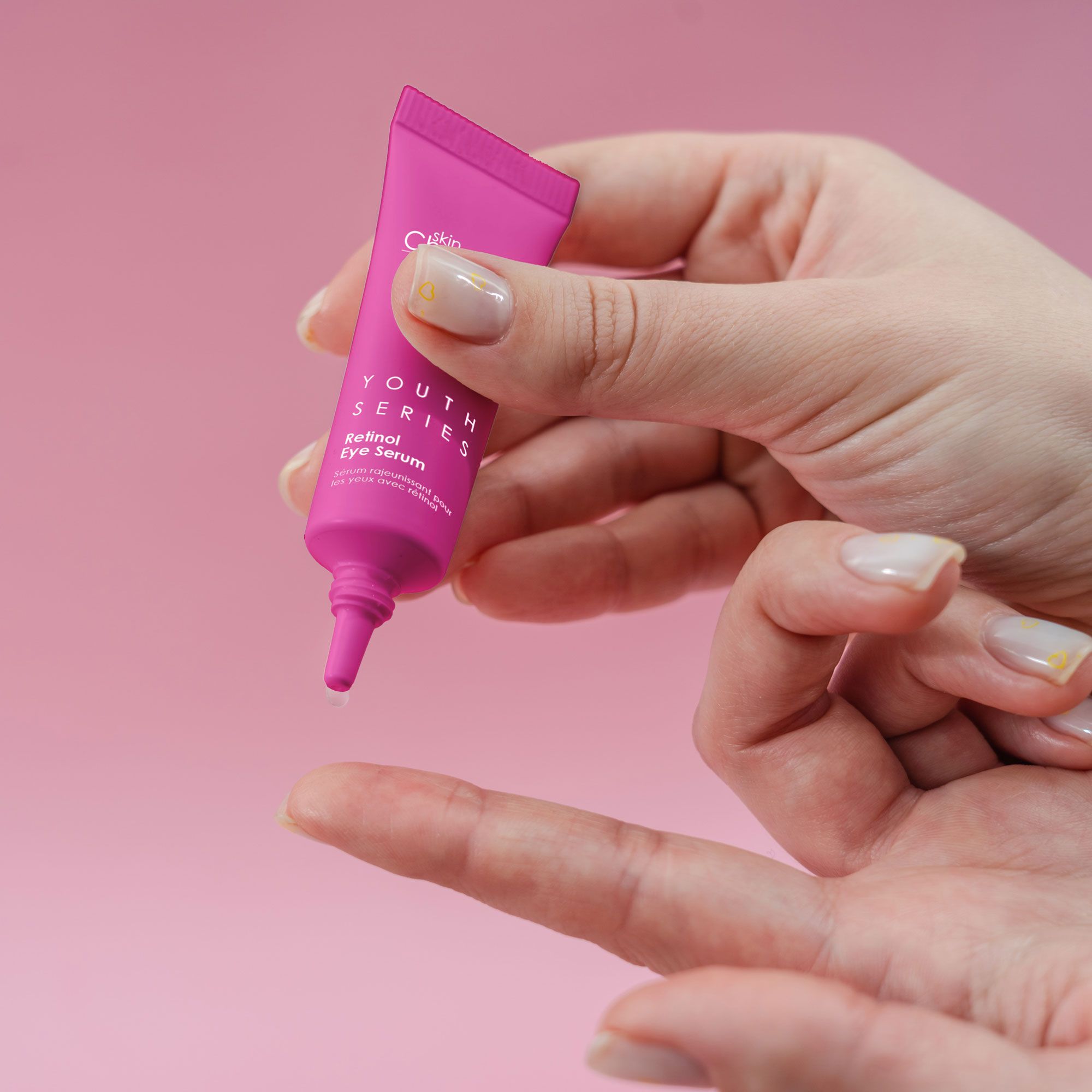 Rosa Tube wird von einer Hand gehalten. Auf dem Tube steht "skinChemists Youth Series Retinol Eye Serum". Rosa Hintergrund.