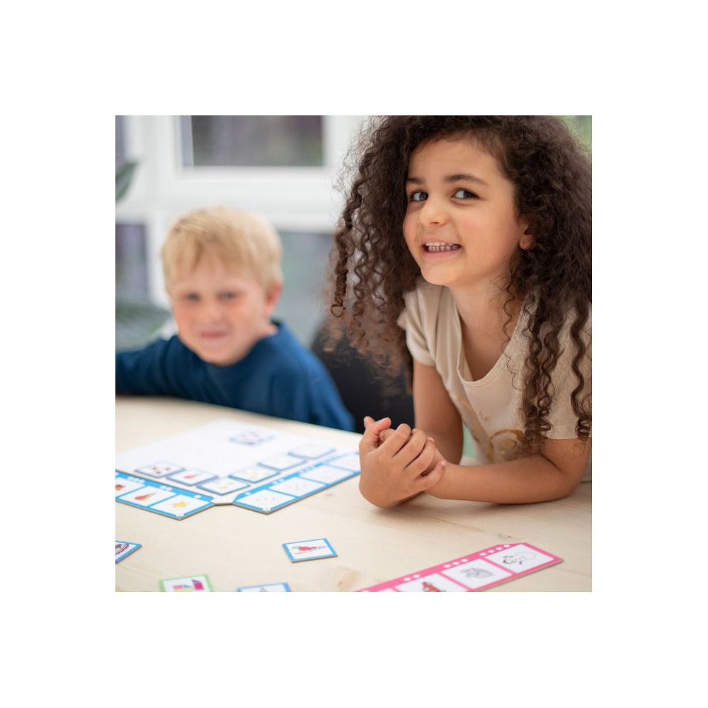 Kinder spielen mit Spielkarten und einem Spielbrett. Auf dem Tisch liegen Karten mit Bildern. Zwei Kinder schauen in die Kamera.