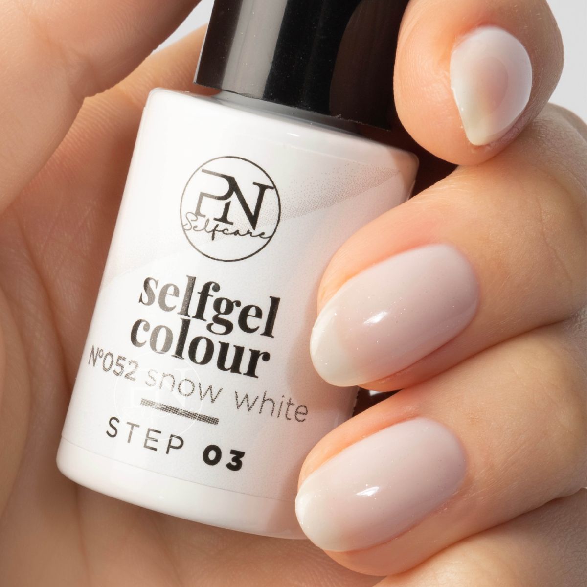 Eine Hand hält eine Flasche Nagellack. Aufschrift: PN Selfcare, selfgel colour, Snow White, STEP 03. Nägel mit hellem Nagellack lackiert.