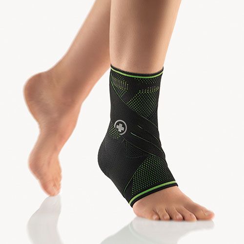 Schwarze Sprunggelenkbandage mit grünen Akzenten. Logo mit weißem Kreuz. Am Fuß getragen.