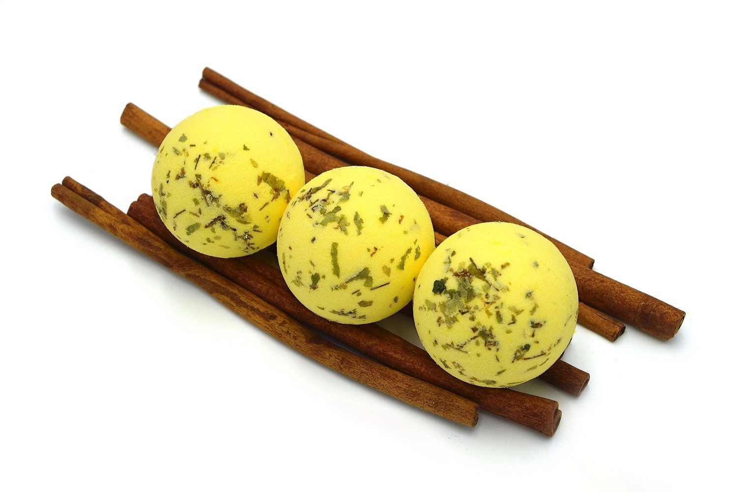 Drei gelbe, runde Badebomben mit grünen Kräutern auf Zimtstangen. Auf weißem Hintergrund.