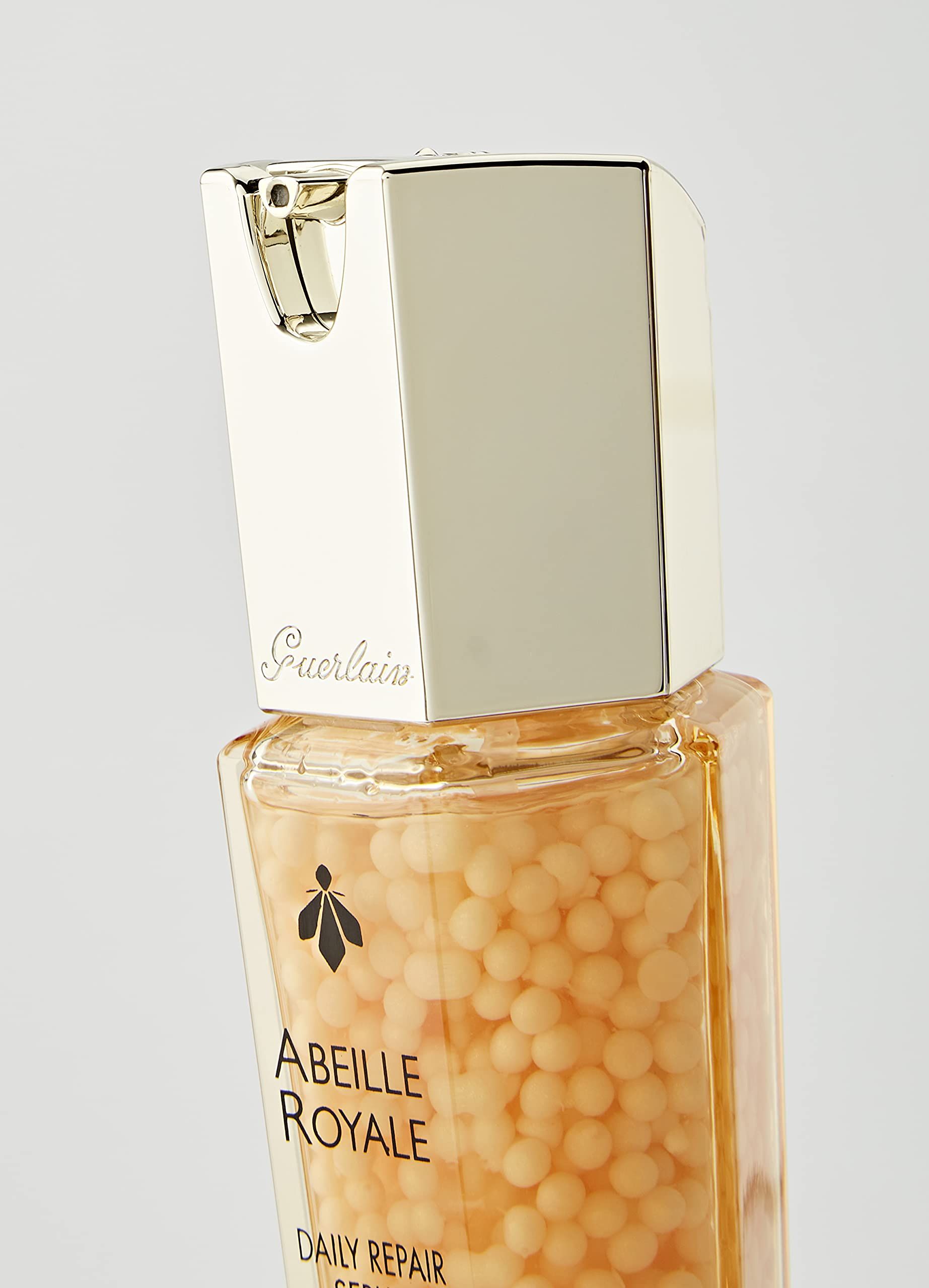 Nahaufnahme der Serumflasche. Aufschrift: Abeille Royale, Guerlain. Goldfarbener Deckel.