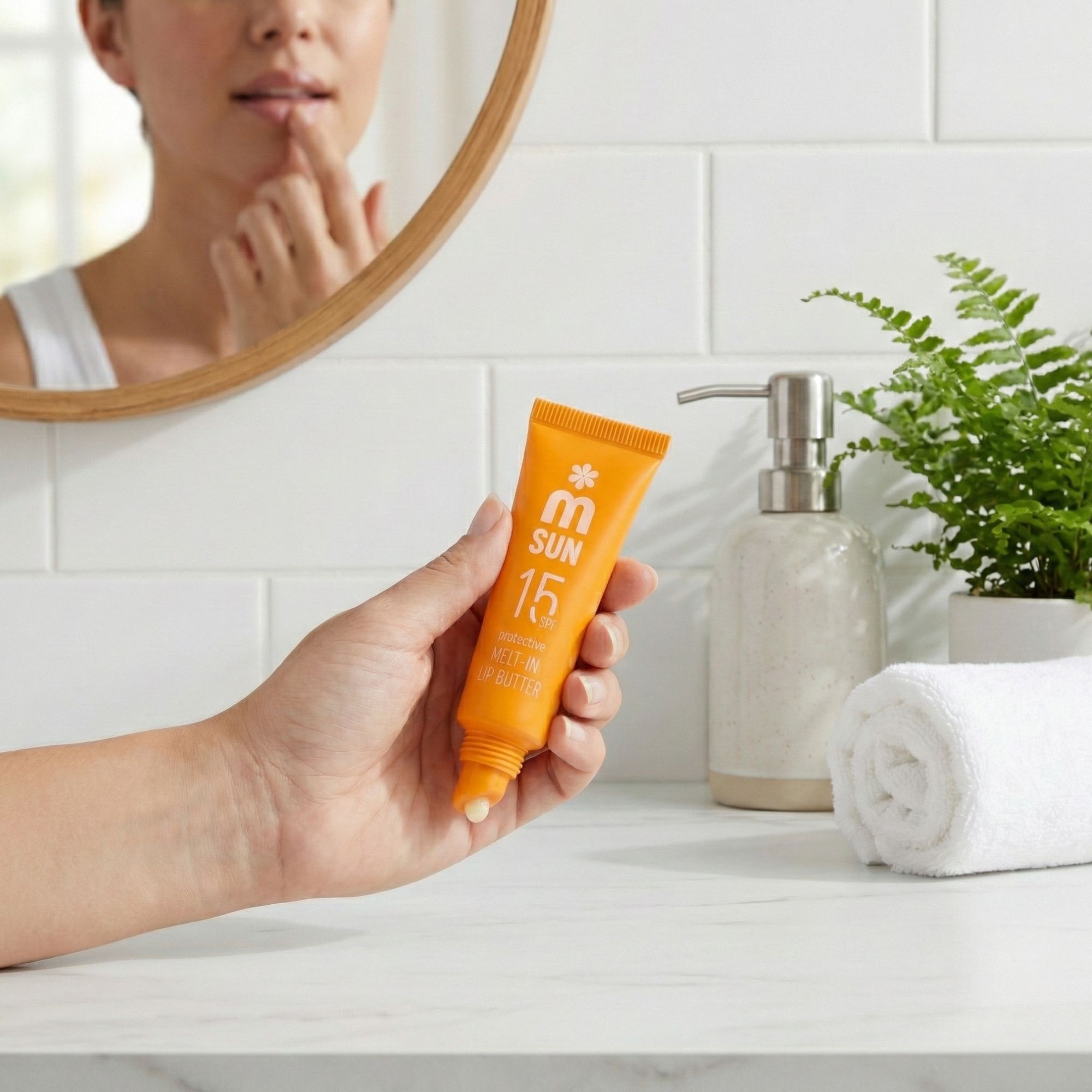 Hand hält orange Lippenbutter-Tube vor Spiegel. Aufschrift: SUN 15 SPF, protective MELT-IN LIP BUTTER. Person berührt Lippen.