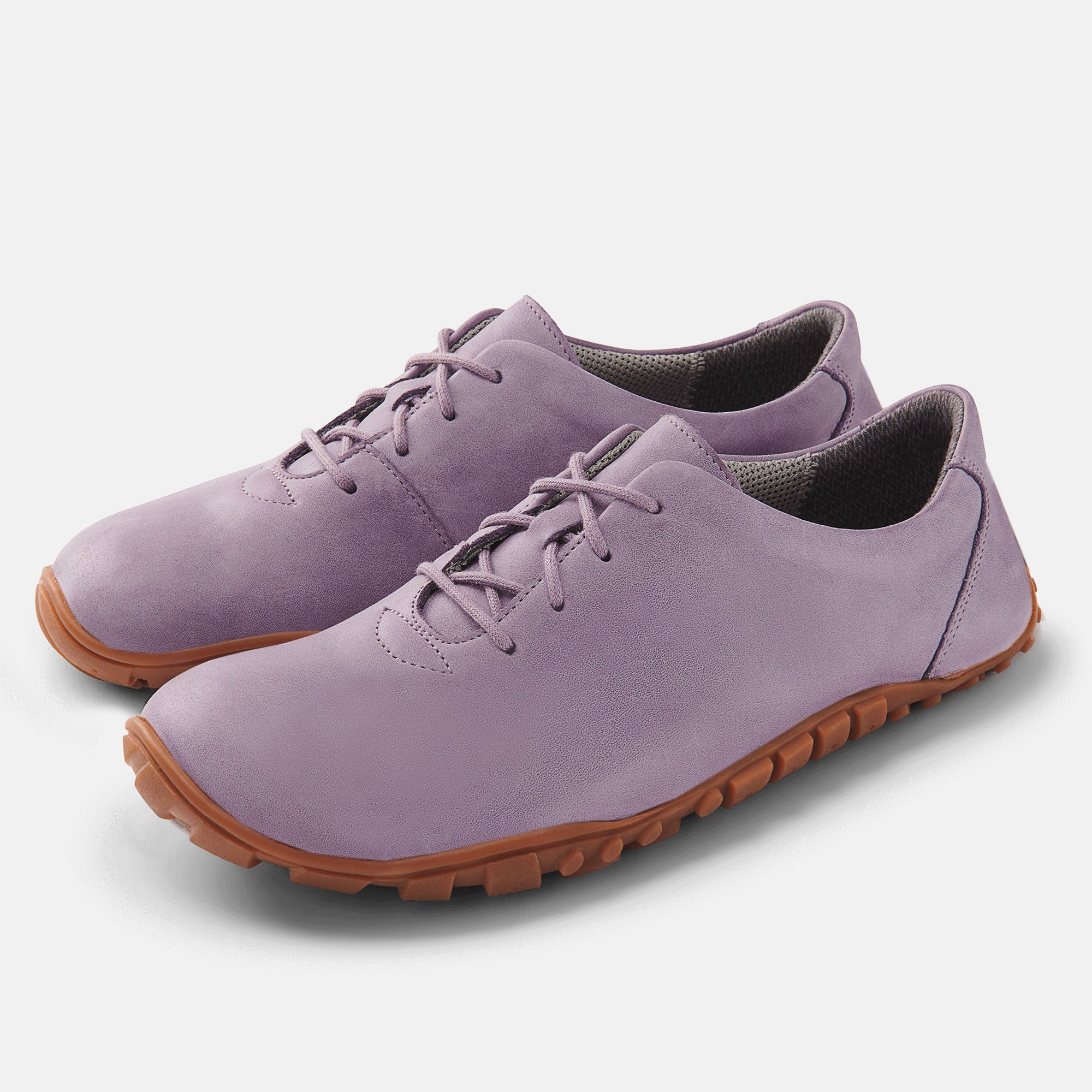 Zwei lilafarbene Schnürschuhe mit brauner Sohle. Breiter Schnitt. Hellgrauer Hintergrund.