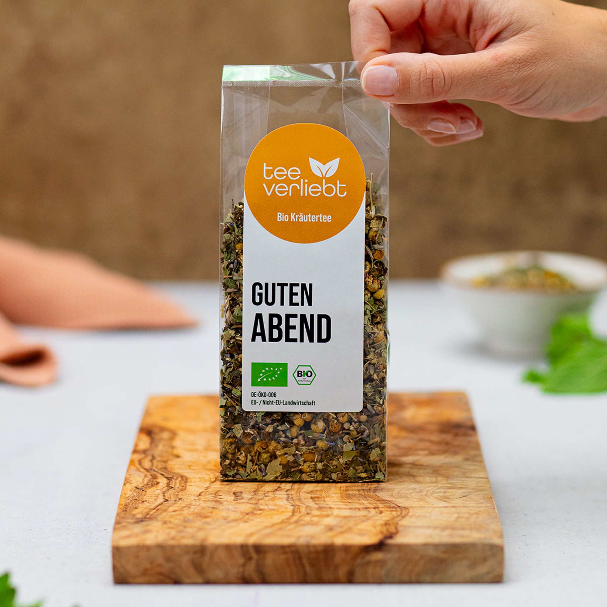 Verpackung mit Kräutermischung. Hand hält Verpackung. Label mit Text 'Guten Abend'.