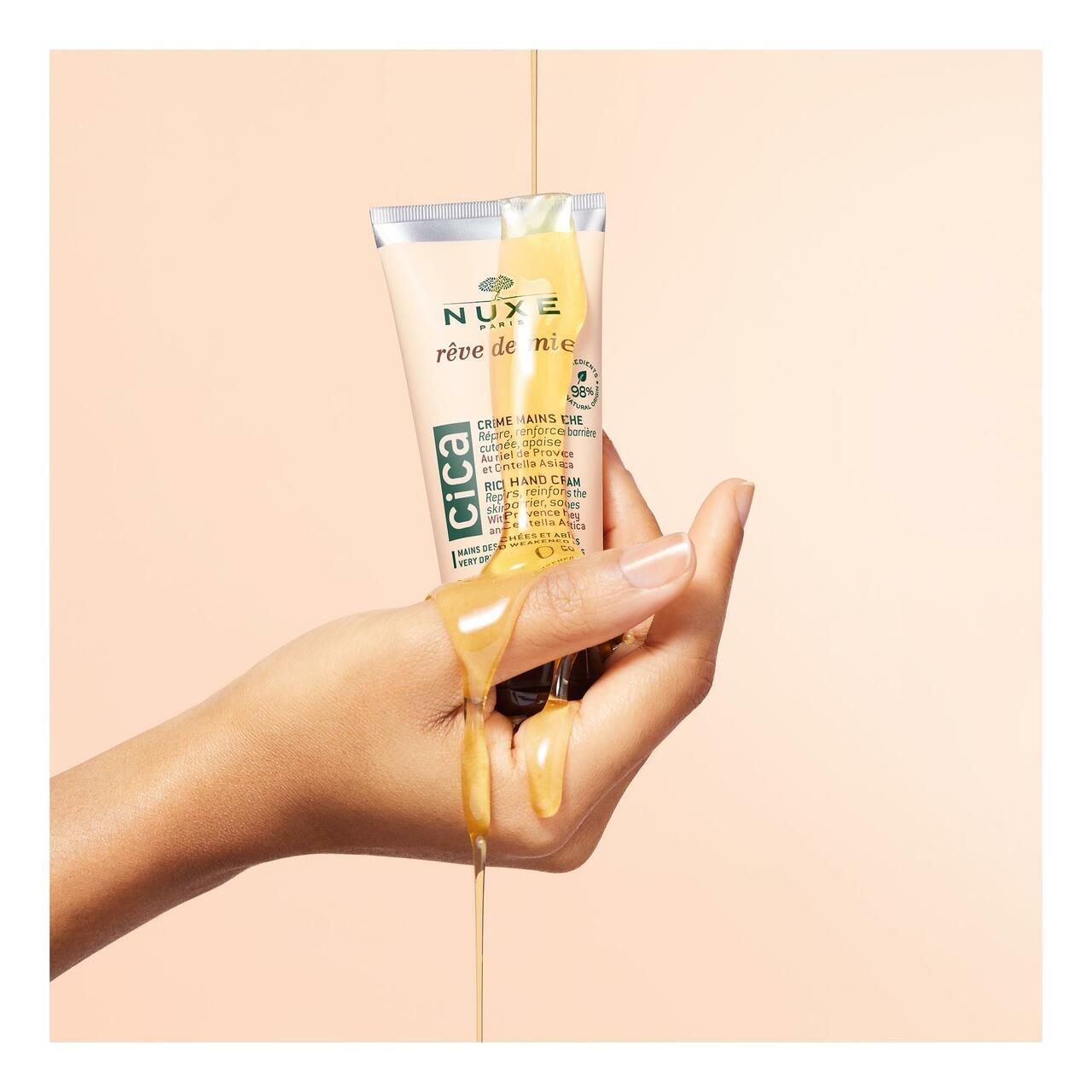 Hand, die Creme aus Tube hält. Honig fließt aus der Tube. Aufschrift: NUXE Rêve de Miel® CICA.
