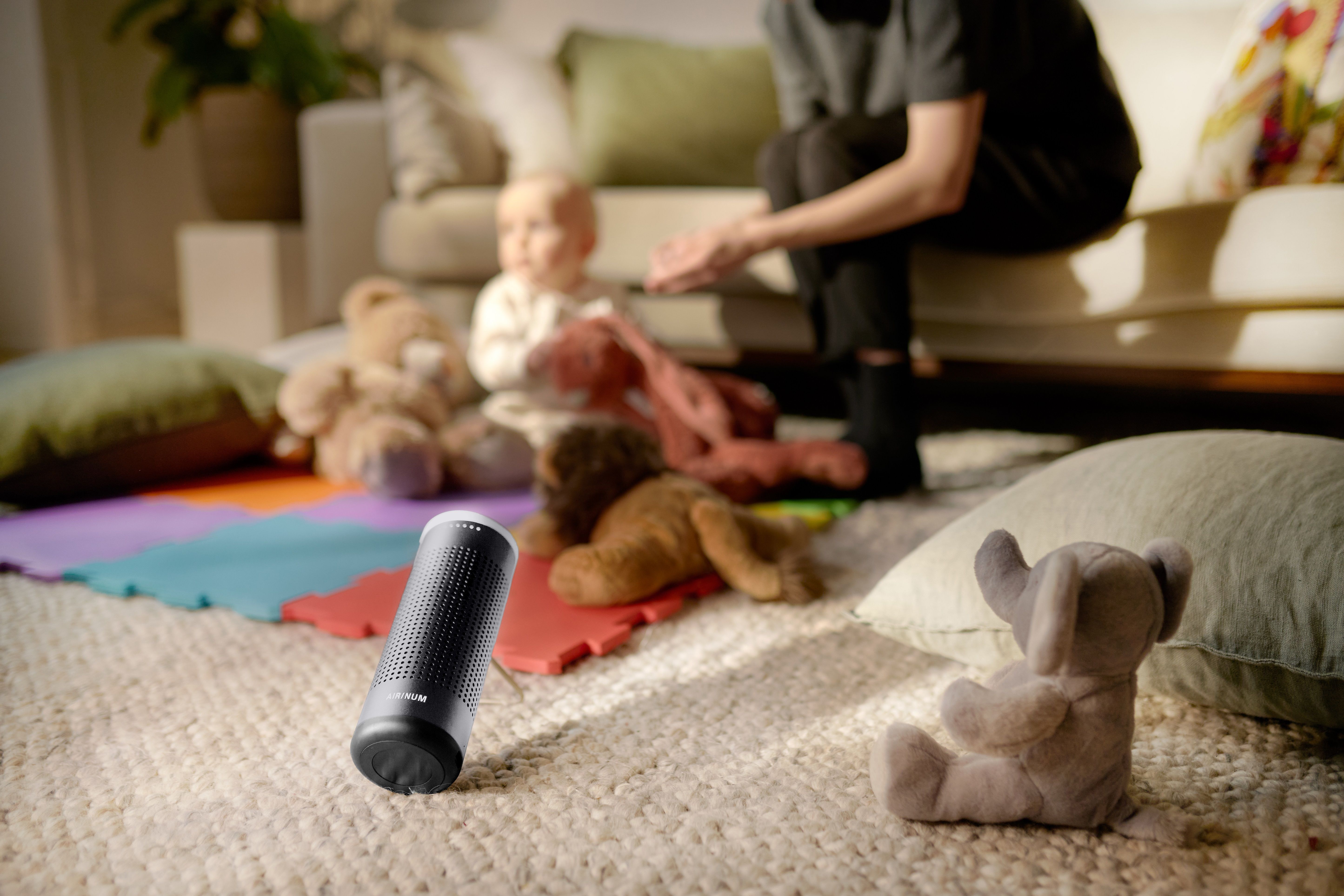 Gerät auf dem Boden, neben Spielzeug und einem Baby. Gerät zylindrisch, schwarz.