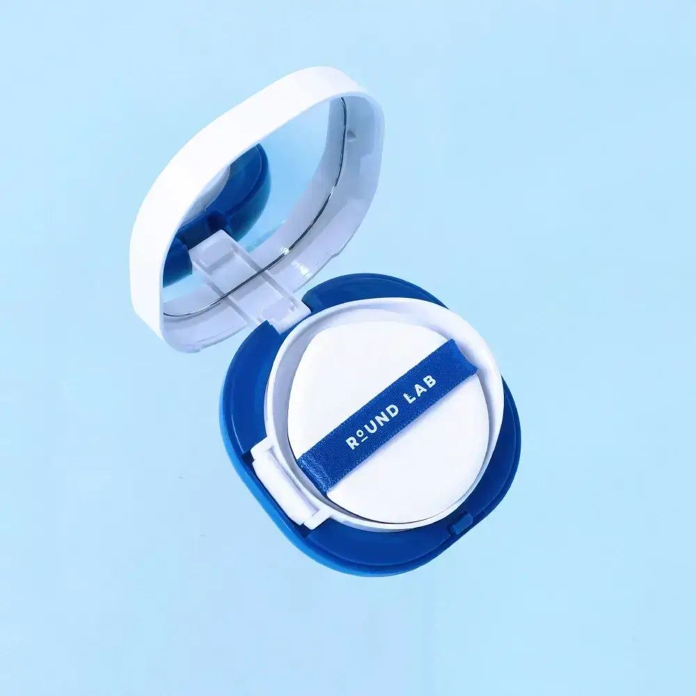 Blau-weiße Kosmetikdose mit Spiegel und Schwamm. Schwamm mit blauem Band und Aufschrift ROUND LAB. Offene Dose.