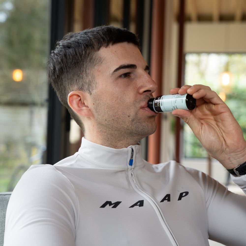 Person trinkt aus einer Flasche mit schwarzem Deckel und Etikett. Auf dem Etikett steht: OLEUS, Recovery.