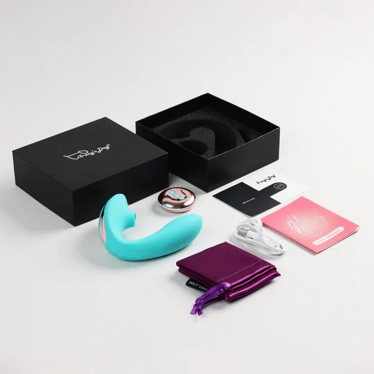 Vibrator, Fernbedienung, Zubehör und Verpackung. Schwarze Box mit Produktname. Mehrere Dokumente und Beutel.