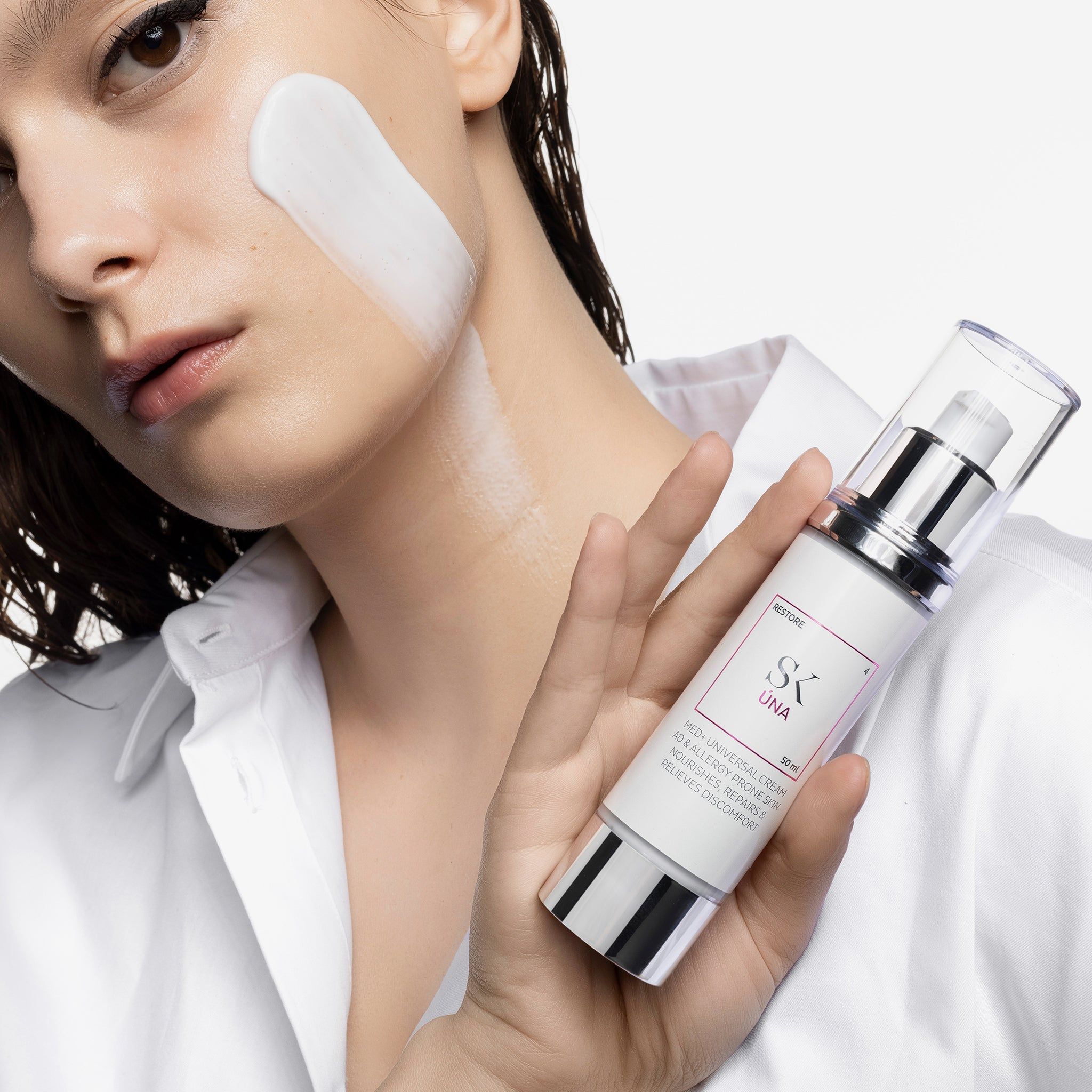 Femme avec crème sur la joue. Tient un flacon de crème. Inscription : SK Úna. Pompe et base argentées.