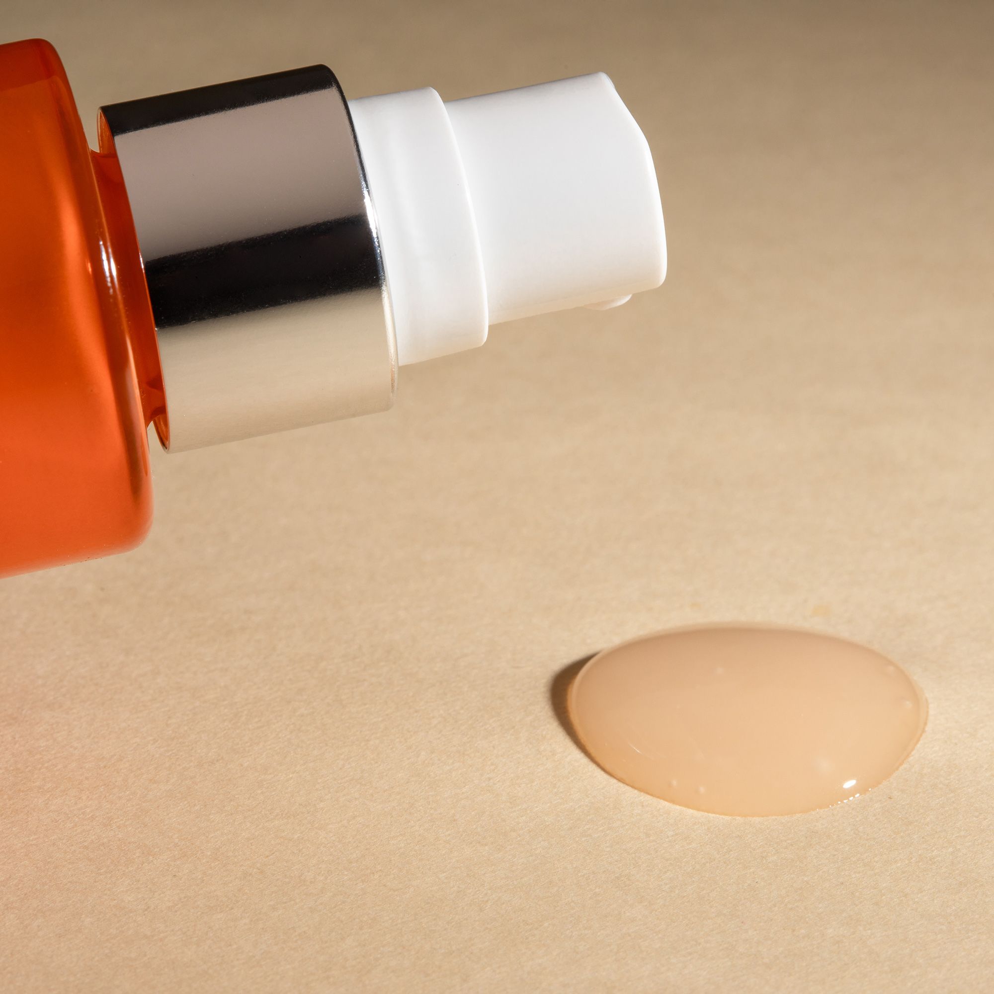 Serumtropfen. Tropfen Serum auf beigem Untergrund. Flasche mit Sprühkopf im Hintergrund.