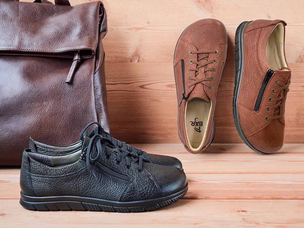 Schwarze und braune Schnürschuhe. Reißverschluss. Leder. Rucksack im Hintergrund.