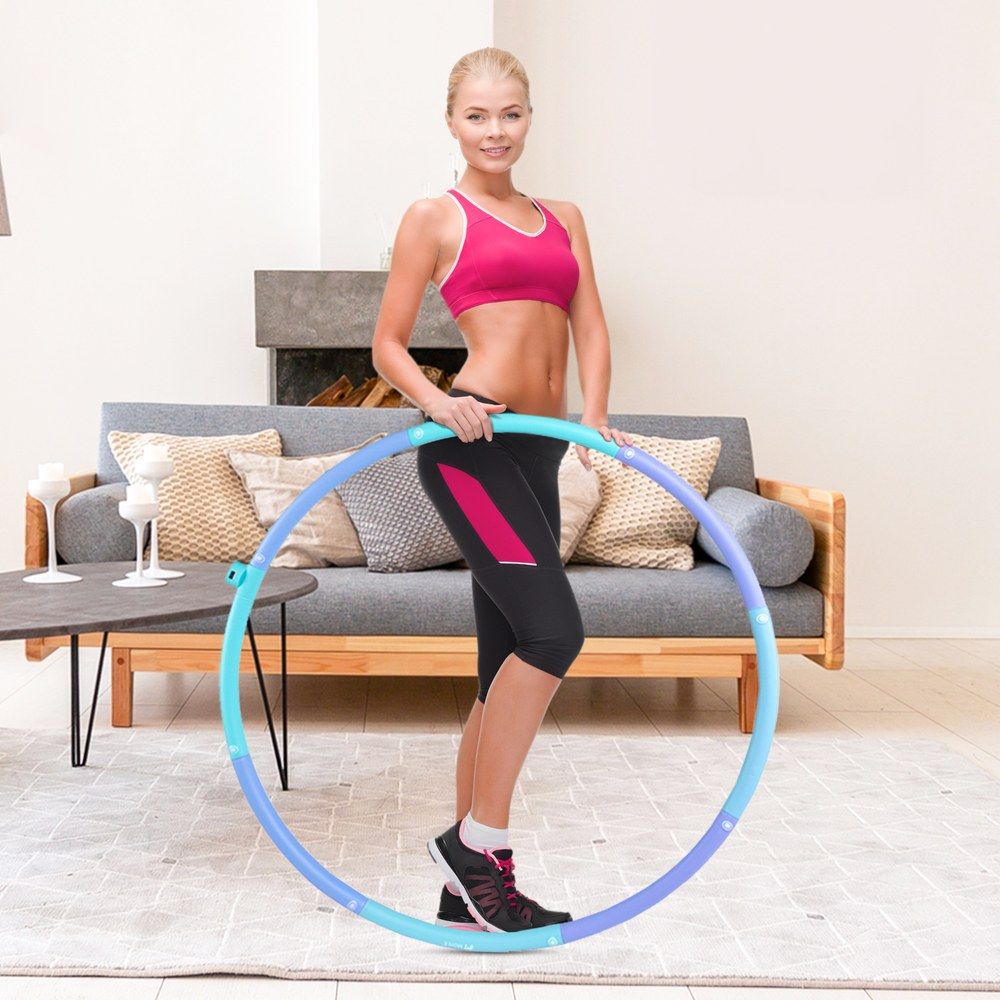Frau mit Hula-Hoop-Reifen in einem Wohnzimmer. Der Reifen ist blau und violett.