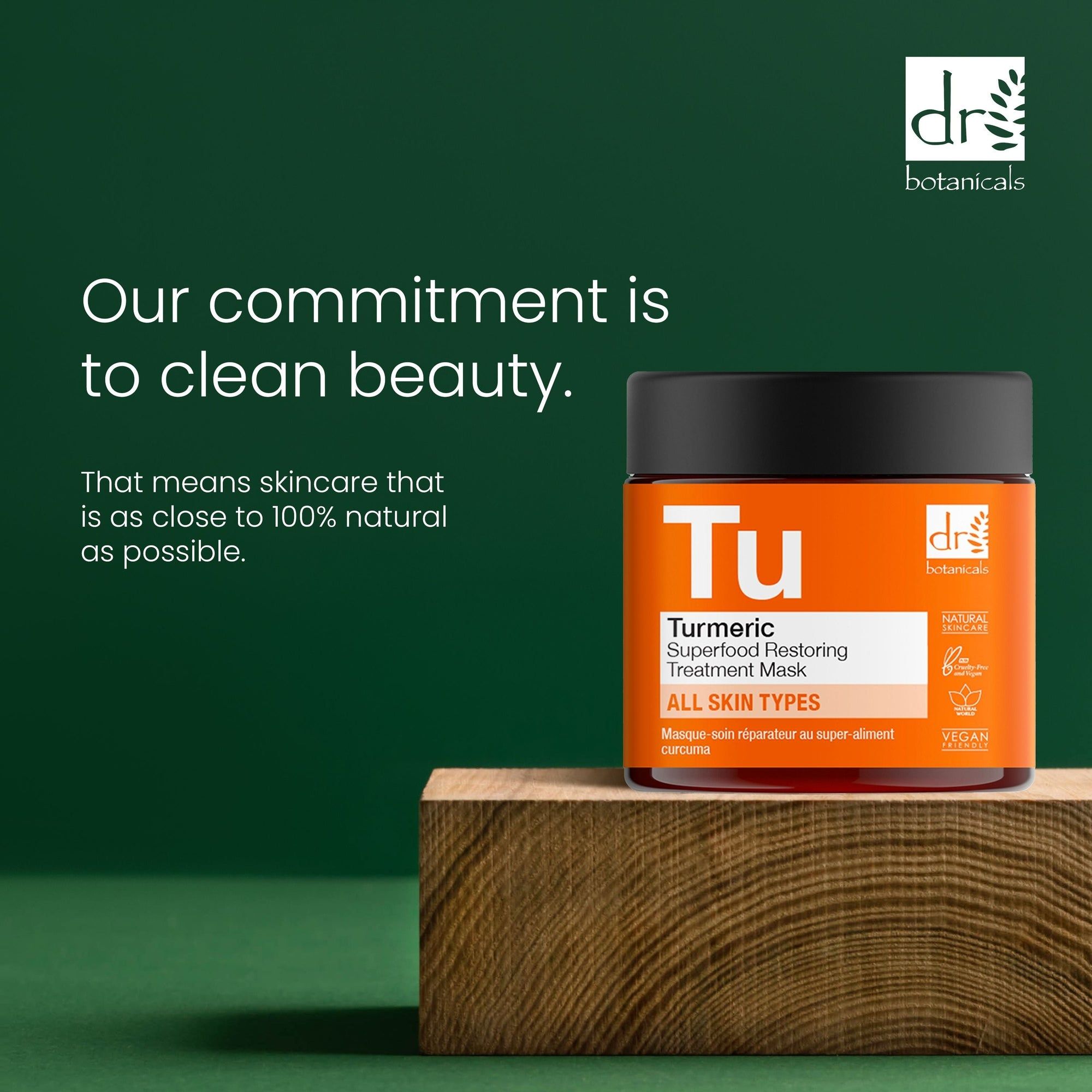 Produkt auf Holzblock. Aufschrift 'Tu' und 'Turmeric Superfood Restoring Treatment Mask'. Orangefarbenes Etikett mit Logo. Text: 'Our commitment is to clean beauty'.