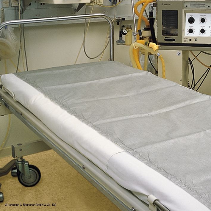 Graues Betttuch auf einem Krankenbett. Das Tuch bedeckt die Matratze. Im Hintergrund medizinisches Gerät.