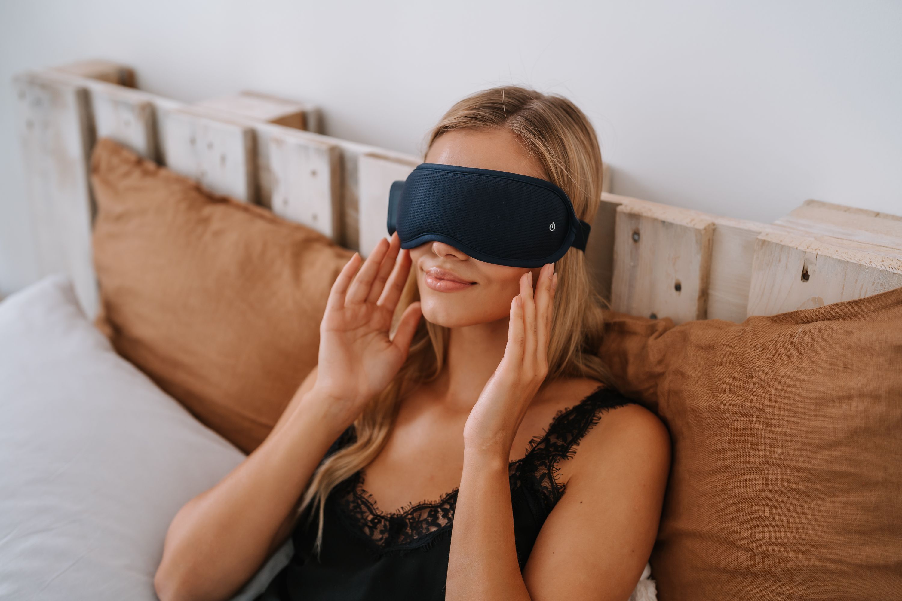 Frau im Bett mit blauem Augenmassagegerät. Hände am Gesicht. Nahaufnahme.