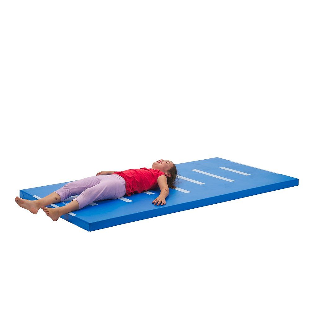 Kind liegt auf blauer Turnmatte mit weißen Streifen. Matte liegt auf weißem Hintergrund.