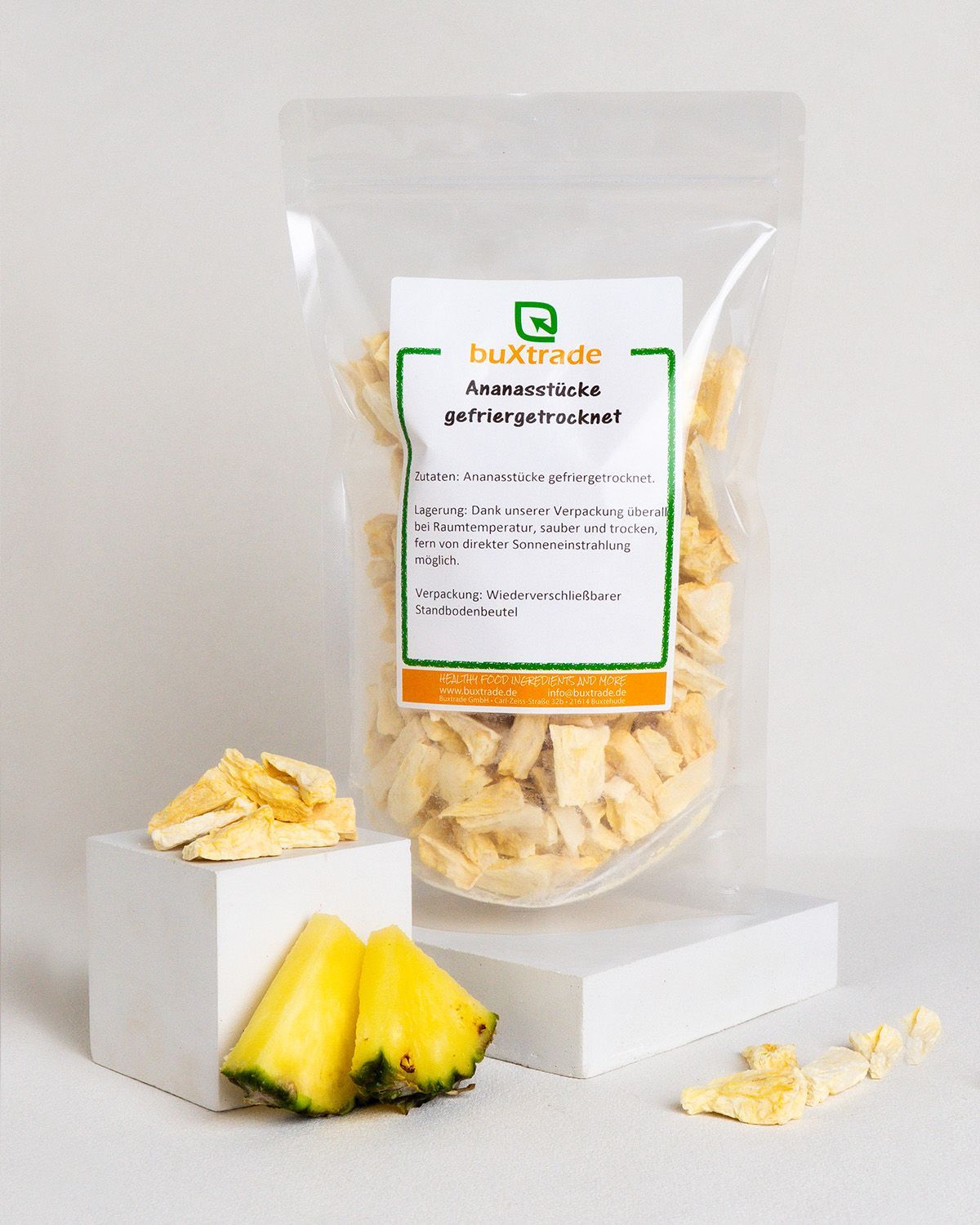 Transparente Verpackung mit Ananasstücken, daneben Ananasstücke und frische Ananasstücke auf weißen Blöcken.