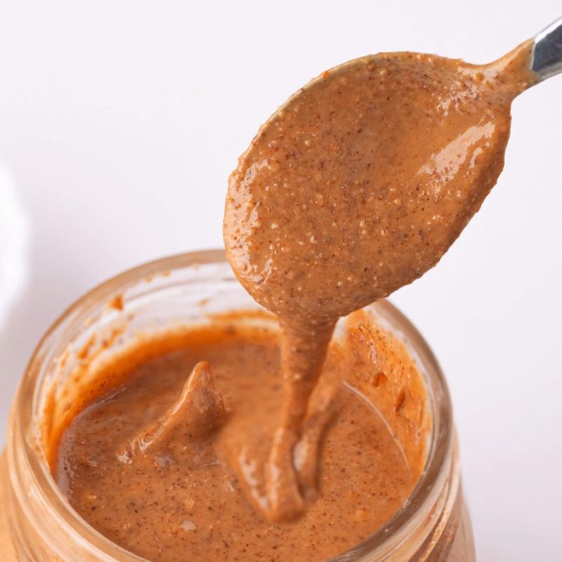 Glas mit Haselnussmus, Löffel mit cremiger Paste. Nahaufnahme, helle Umgebung.