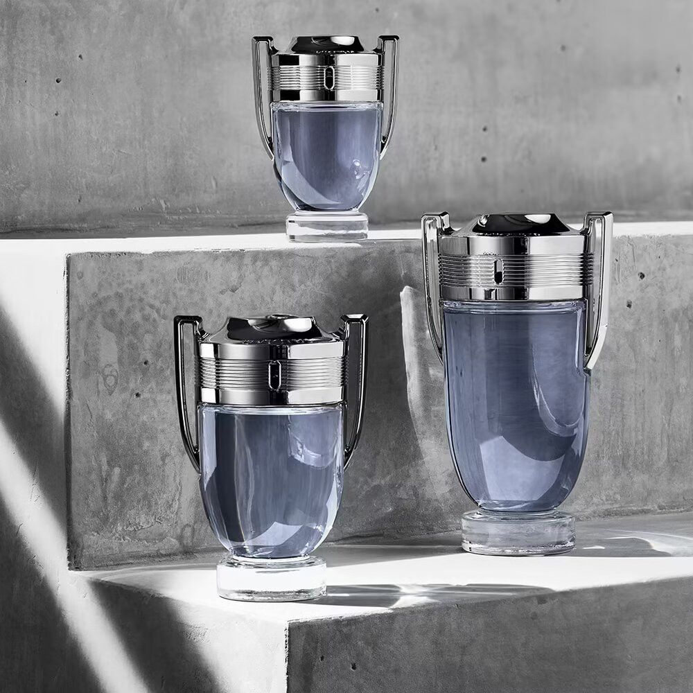 Drei INVICTUS-Flakons mit silbernen Deckeln auf einer grauen Oberfläche. Unterschiedliche Größen.