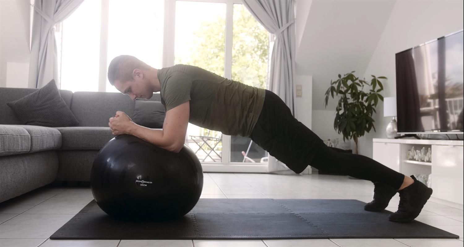 Mann trainiert auf einem schwarzen Gymnastikball. Er stützt sich auf den Unterarmen.
