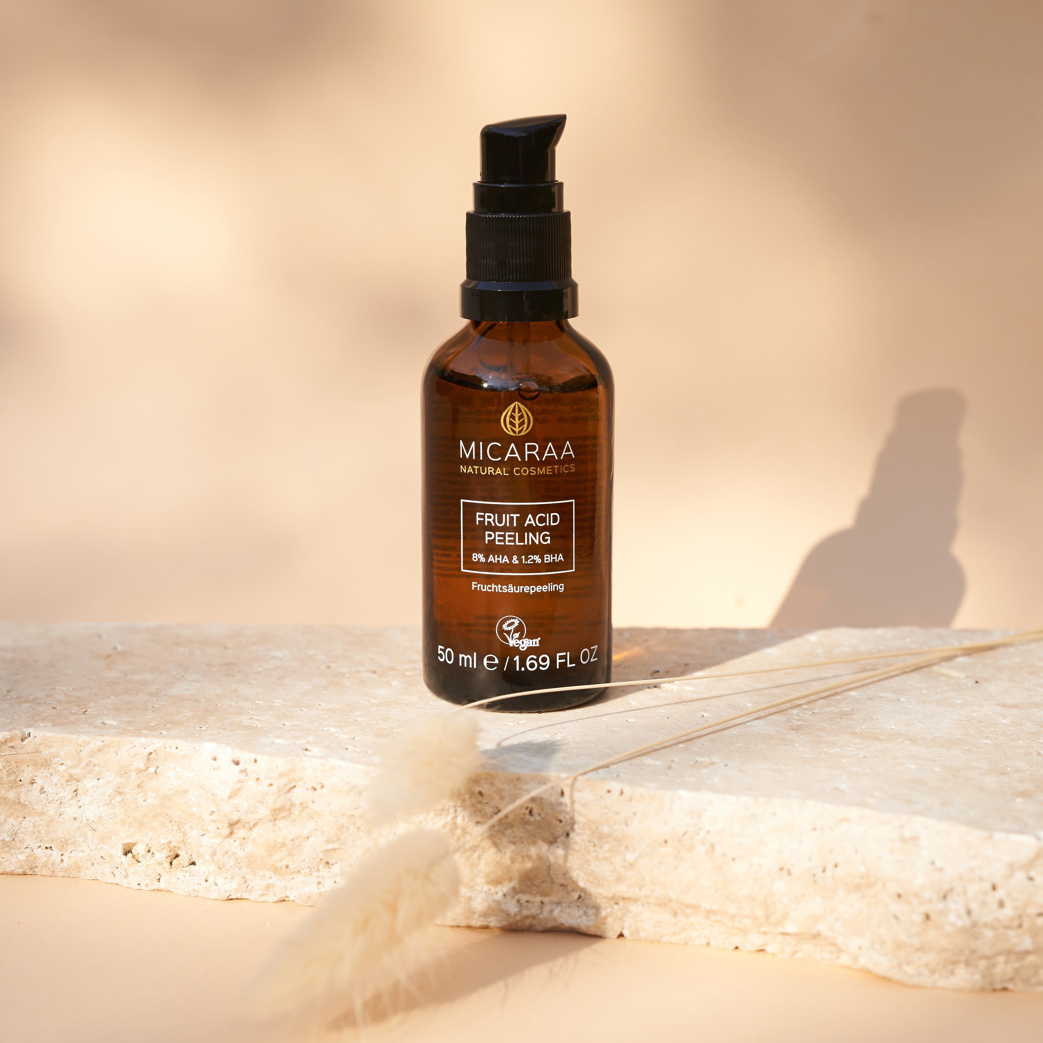 Braune Glasflasche mit schwarzem Pumpkopf auf Stein. Beschriftung: MICARAA, Fruit Acid Peeling, 8% AHA & 1.2% BHA, vegan. 50 ml.