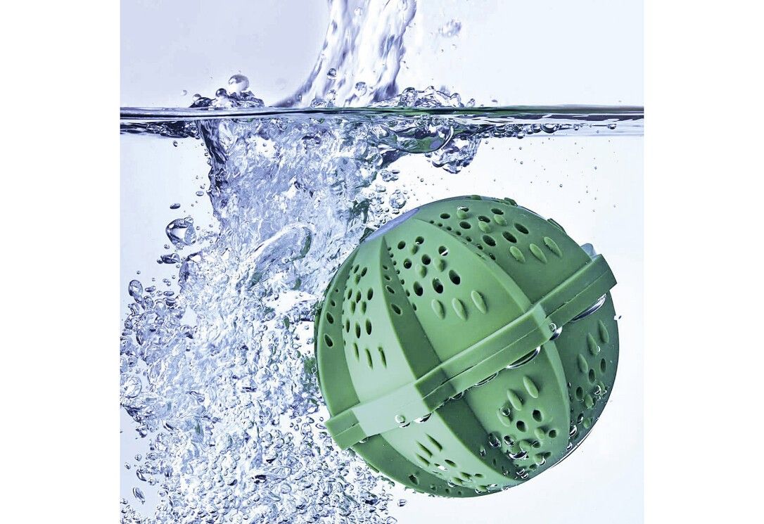 Grüner Waschball im Wasser. Wasser spritzt und bildet Blasen. Der Ball hat Löcher.