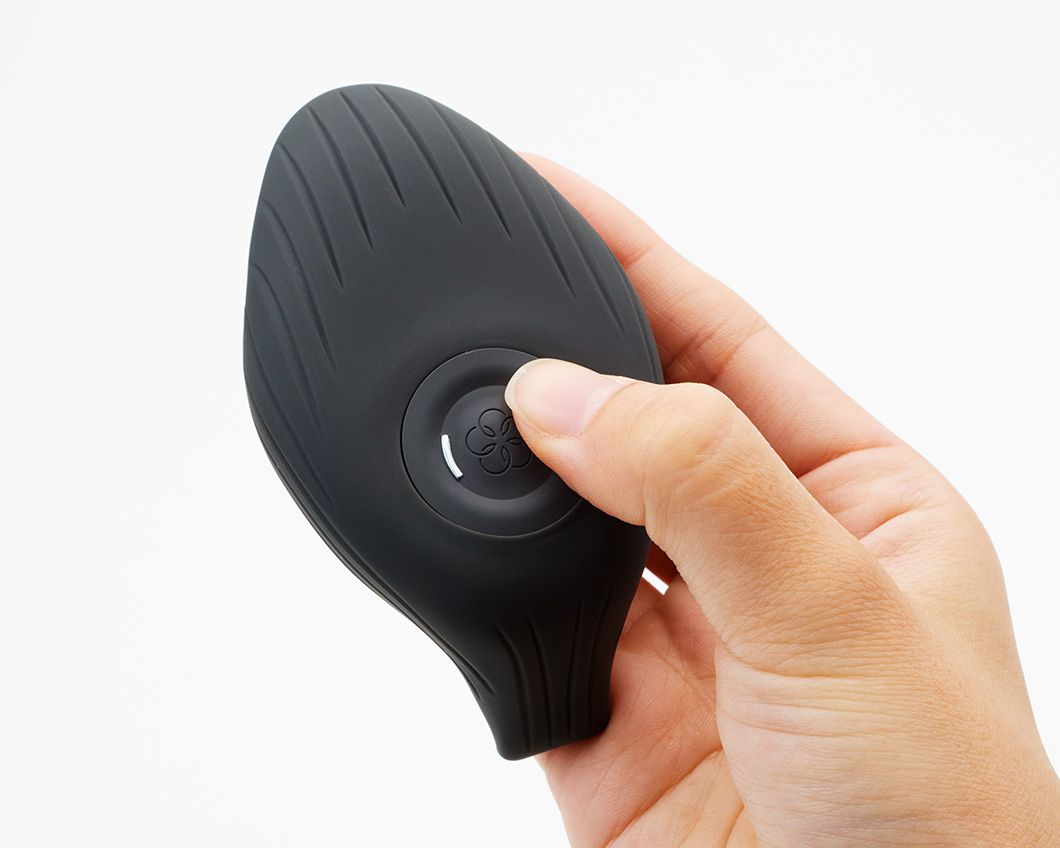 Schwarzer Vibrator mit Knopf. Organische Form mit geriffelter Oberfläche. In Hand gehalten.