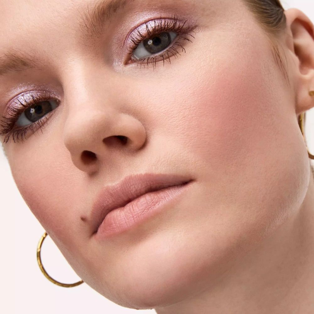 Nahaufnahme eines Gesichts mit rosa Lidschatten. Sichtbar sind Augen, Lippen und Wangen. Goldene Ohrringe.