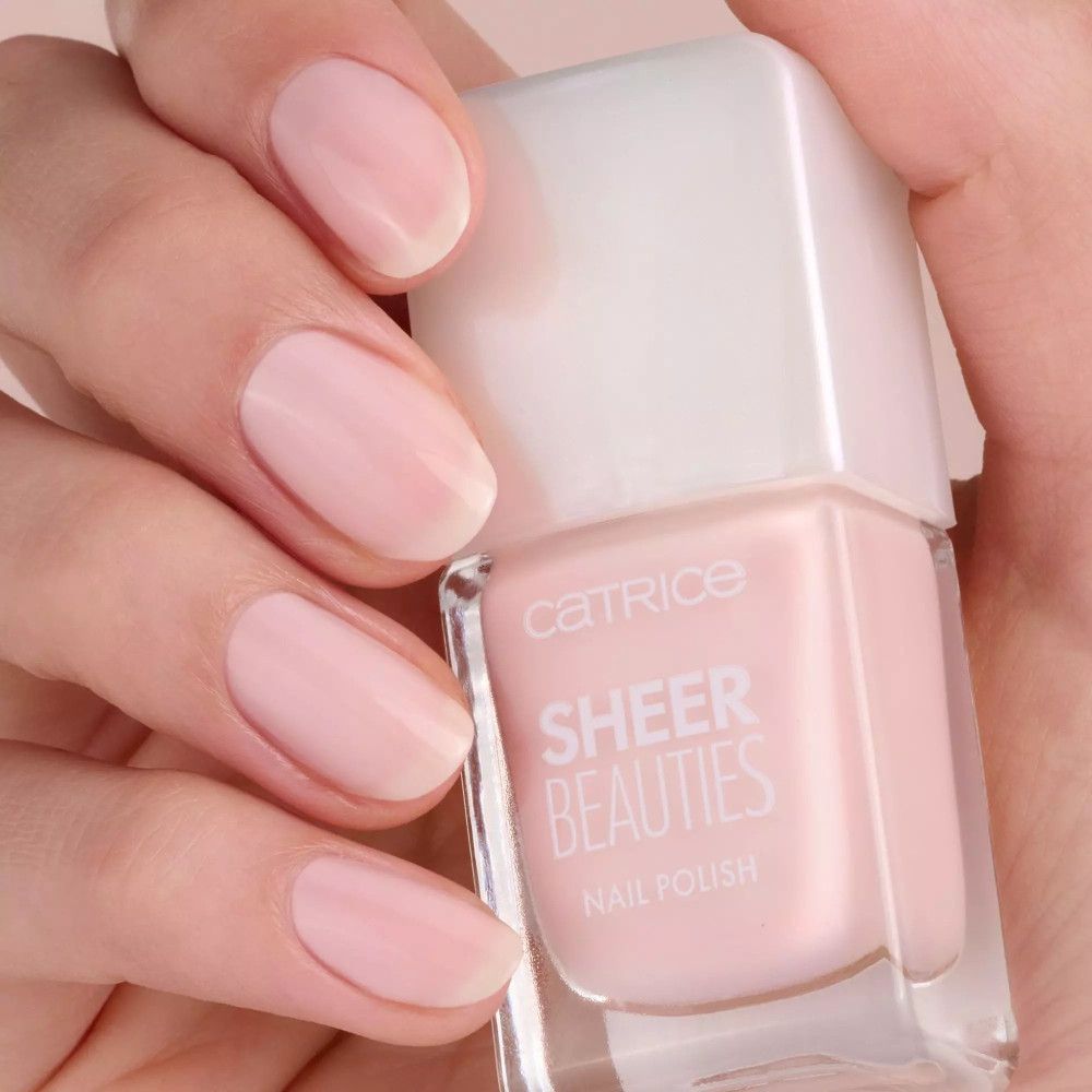 Hand mit lackierten Nägeln und Nagellackflasche. Aufschrift: Catrice Sheer Beauties Nail Polish. Rosa Farbe.