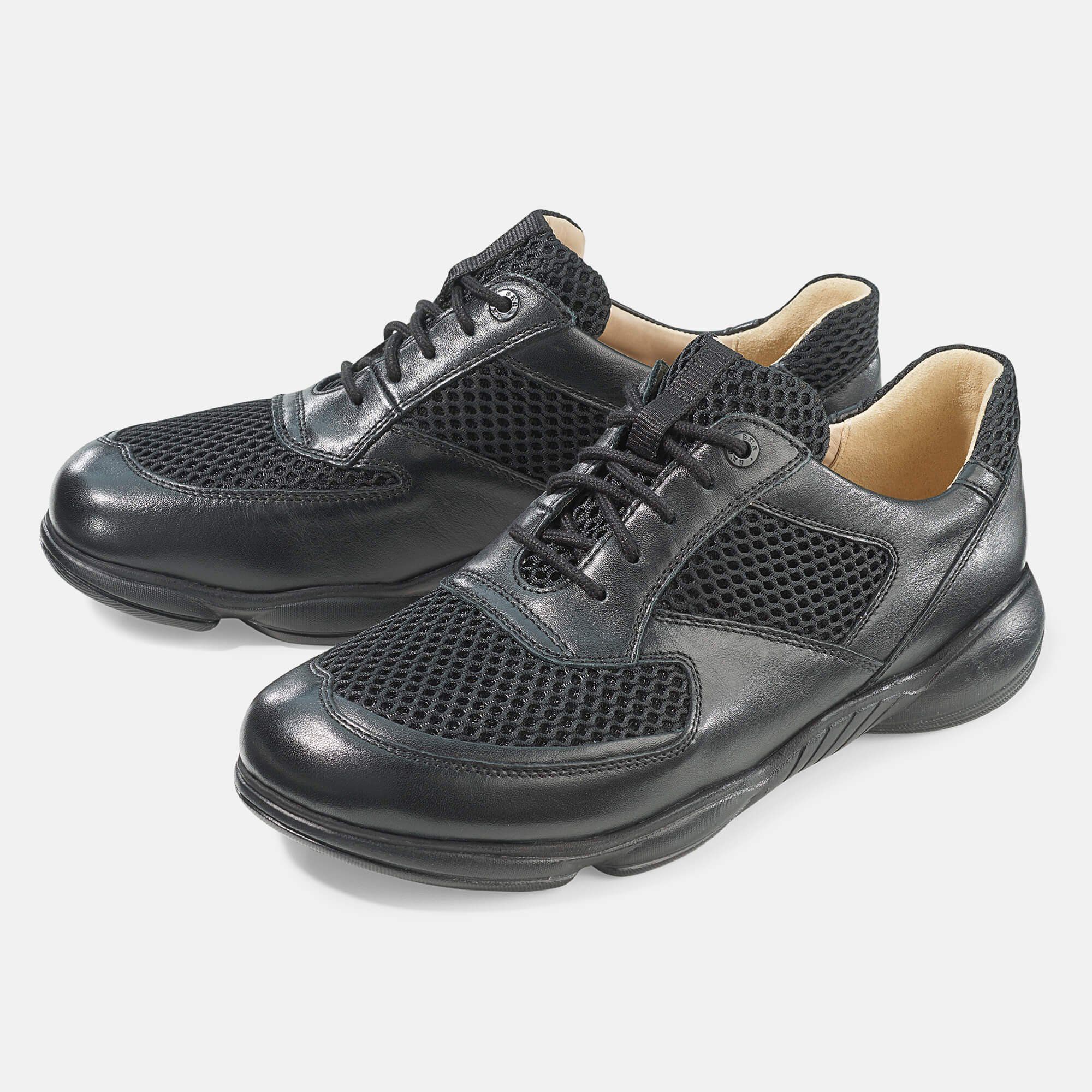 Schwarzer Schnürschuh mit Mesh-Einsatz. Breite Passform. Leder und Textil. Hellgrauer Hintergrund. Schuh leicht schräg gestellt.