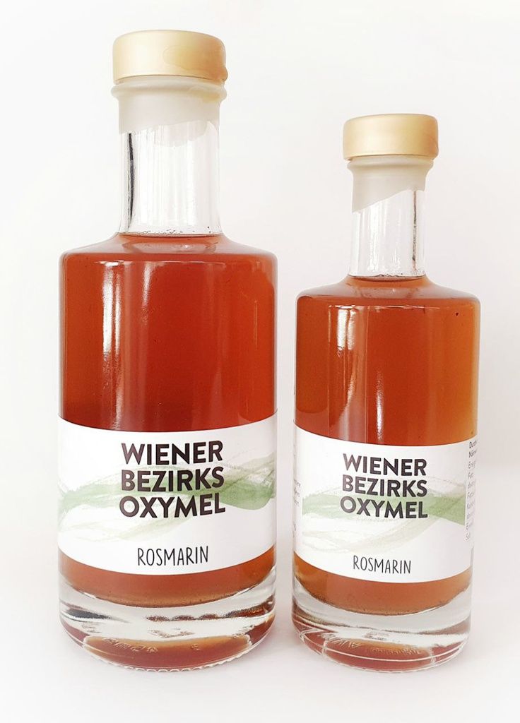 Zwei Glasflaschen mit Etiketten. Aufschrift: Wiener Bezirks Oxymel Rosmarin. Helle Flüssigkeit, goldfarbene Verschlüsse.