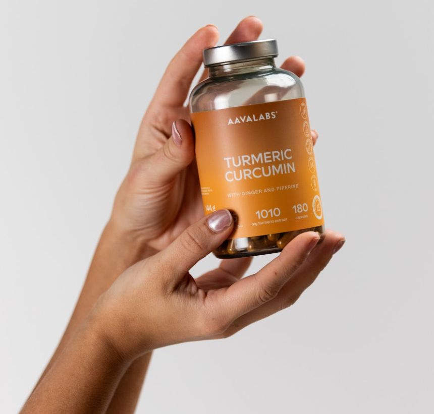 Hände halten eine Flasche mit Kurkuma-Kapseln. Das Etikett zeigt 'Turmeric Curcumin'.